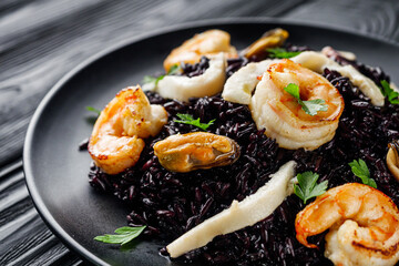 delicious black rice with shrimps and seafood on a black wooden rustic background