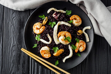 delicious black rice with shrimps and seafood on a black wooden rustic background