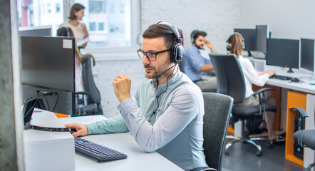 Handsome customer service support operator man with headphones and microphone using computer in...