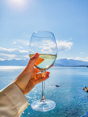 A glass of white wine in a girl's hand against the backdrop of the sea and mountains