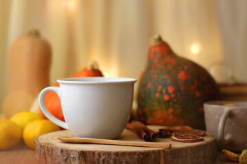 Cup of tea or coffee, seasonal spices, bowl of cookies, blanket, pumpkins, colorful leaves, books and tangerines on wooden table. Cozy hygge at home. Selective focus.