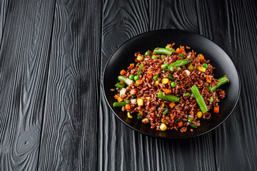 delicious red rice with vegetables on a black wooden rustic background