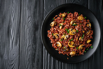 delicious red rice with mushrooms on a black wooden rustic background