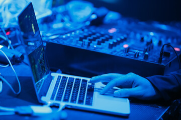 Club dj playing music with mixing software on laptop in night club. Nightclub disc jockey mixes musical tracks on notebook