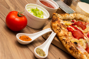 Tasty pizza with pepperoni, ham and peppers and pizza ingredients around the table