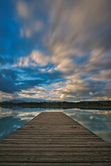 Vertical shot of a wooden pontoon against a lake with reflection of beautiful cloudy sky on it