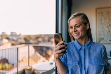 Happy blonde woman, holding a mobile phone, looking at it.