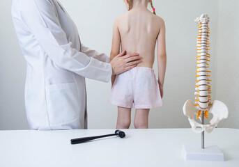 A pediatric neurologist doctor examines the back of a 5-year-old girl who has back pain. Treatment of muscle pain and scoliosis in children - obrazy, fototapety, plakaty