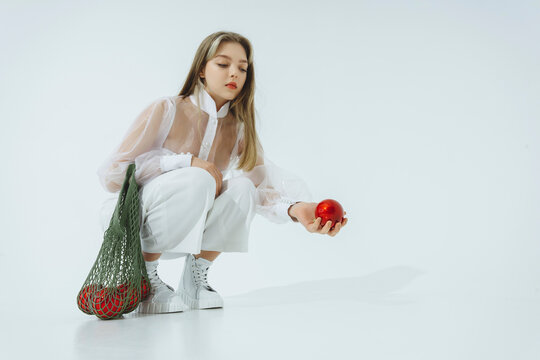Teenage girl holding Christmas ornament crouching against white background