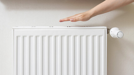 The girl holds her hand near the radiator in the room. The concept of comfortable temperature in...
