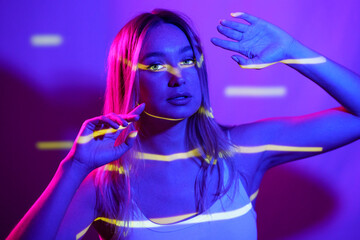 Young woman with neon colored lighting in front of wall