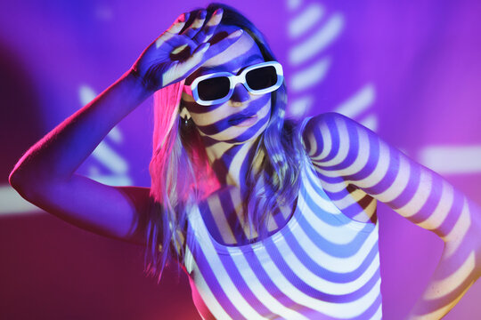 Woman wearing sunglasses with neon colored lights in front of wall