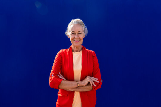 Smiling mature woman with arms crossed in front of blue wall