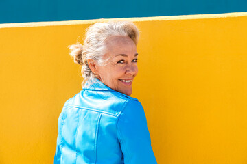 Happy mature woman looking over shoulder in front of wall