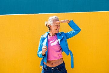Smiling mature woman shielding eyes in front of colored wall
