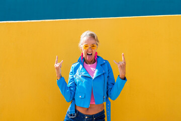 Mature woman sticking out tongue in front of colored wall