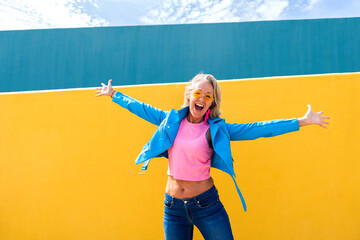 Happy mature woman with arms outstretched in front of colorful wall