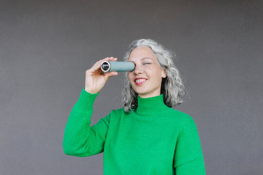 Smiling woman looking through monocular in front of wall