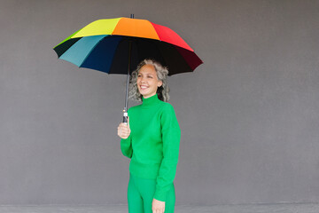 Happy woman with colorful umbrella standing in front of wall