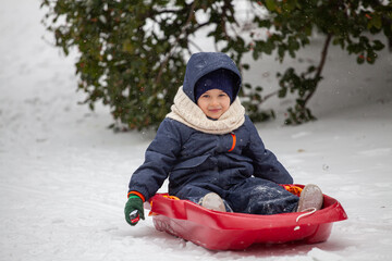 Happy little boy on his sled in winter snow