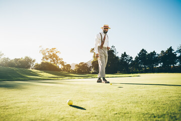 View of an elegant mature African American male golfer in a fashionable outfit with suspenders,...