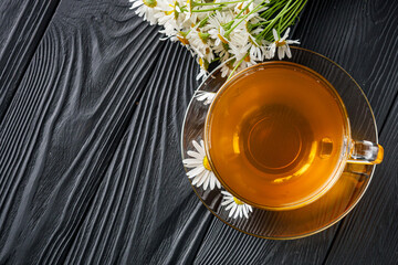 aromatic hot chamomile tea on a black rustic wooden background