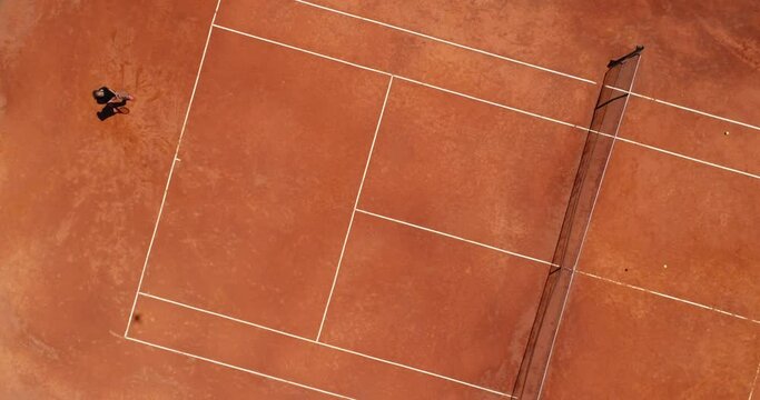 Aerial top view of a young female tennis player playing on brown ground court. Professional girl tennis player hitting a backhand on court Flat layout sport background. 