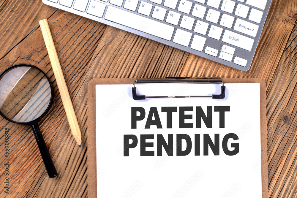 Poster patent pending text on paper clipboard with magnifier and keyboard on wooden background