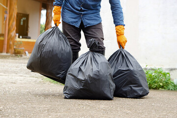 Closeup man holds black plastic bag that contains garbage inside, stand in front of house. Concept...