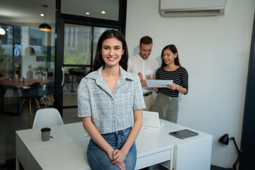 Portrait of businesswoman working and looking camera with business team behind in a meeting room.	