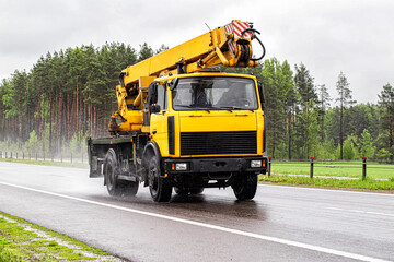 Fototapeta na wymiar a yellow truck crane rides along an asphalt road outside the city in rainy weather against the backdrop of a forest. Crane rental