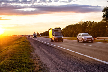 Fototapeta na wymiar A van transports cargo on a motorway in the summer against the backdrop of a sunny sunset in the evening. The concept of cargo transportation on vans, mobility and speed of cargo delivery. 