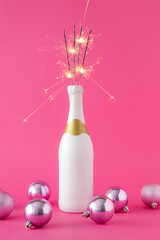Christmas creative layout with bottle of champagne, sprinkles and pink Christmas balls against pink background. New year party celebration concept.