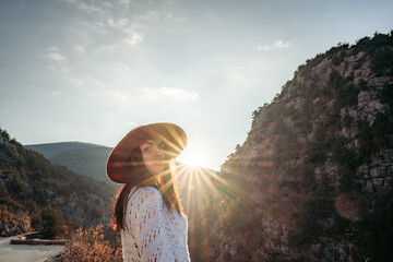 Traveler woman in brown hat and white sweater looking at amazing mountains and forest, wanderlust...