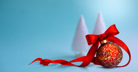 Art Close-up of a red Christmas bauble tied with ribbon and Christmas tree on a table. Banner or...