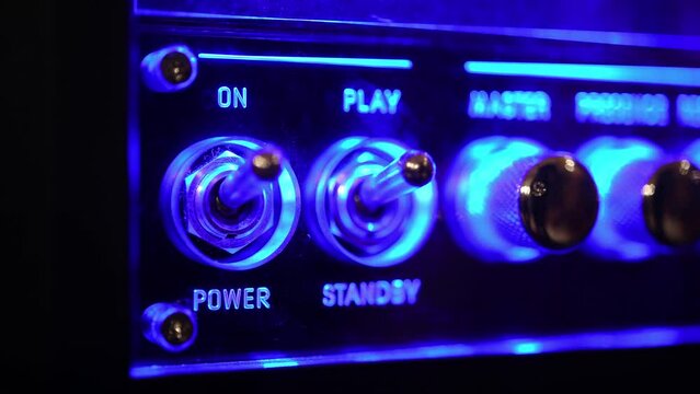 Power on and play toggle on electric equipment with blue glow light, human hand switch button detail on music amplifier control panel
