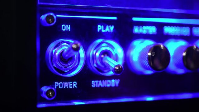 Power on electric equipment with blue glow light, human hand using analog toggle switch detail on music amplifier control panel