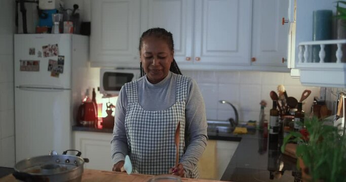 Happy senior african woman dancing to music playlist while baking inside kitchen at home