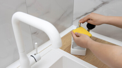 A girl applies an anti-grease detergent to a dishwashing sponge. White beautiful water faucet and modern sink.