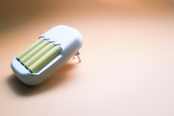 Charger and Batteries. Charger with yellow AA accumulator, on orange background