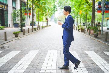 コーヒーを片手にオフィス街を歩くビジネスマン