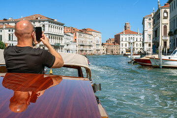 Fototapeta na wymiar A young man holds a smartphone in his hands on the island of Venice in Italy on a sunny day while traveling by boat. Mobile communications while traveling, mobile photography and videography