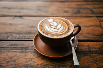 A cup of cappuccino with a beautiful pattern in the foam photographed on a rustic wooden table.
