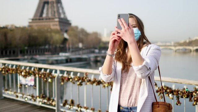 Girl near Eiffel tower in Paris wearing mask and taking selfie or recording video blog during coronavirus outbreak