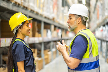 senior male manager explains warehouse work to a female Asian employee who checks inventory in the...