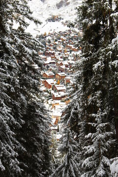Verbier village. Traditional Alpine Village full of Swiss Chalets in the mountains. Seen between tall snow covered evergreens huddled in a mountain valley. Adorable winter travel Christmas concept 