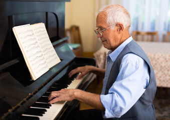 Grandfather is learning to play piano at home. Life after retirement concept © caftor