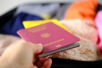 close-up of women's passport, covid certificate, folded clothes in open suitcase, woman packing...
