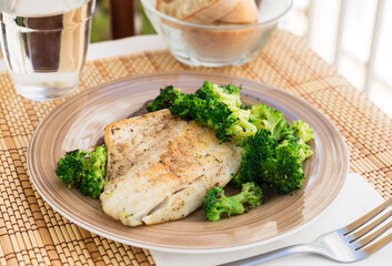 fried fillet of sea bass with garnish of broccoli on black warm stone plate