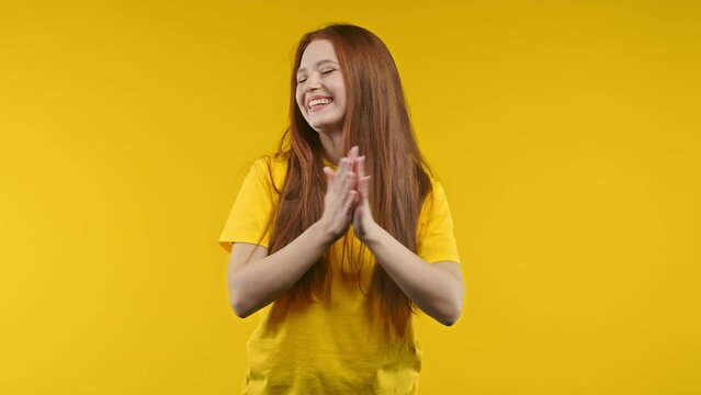 Happy ginger woman applauding on yellow background. Smiling lady emotional claps hands, congratulating. Support, cheering, gratitude concept